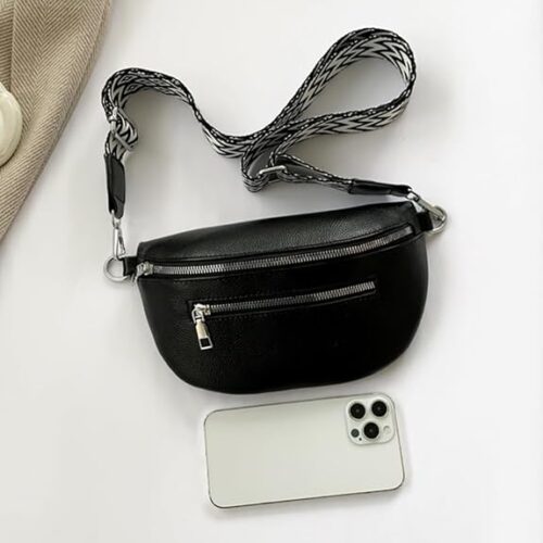 Eine Bauchtasche Damen Leder, eine kleine wasserabweisende Gürteltasche aus schwarzem Leder mit zwei Reißverschlusstaschen und gemustertem Riemen, liegt auf weißer Fläche neben einem weißen Smartphone mit drei Rückkameras.